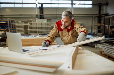 Mid adult carpenter checking measurements and writing notes on the paper while working in a workshop.